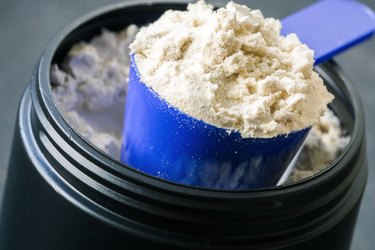 Scoop of whey protein powder on a protein powder container.
