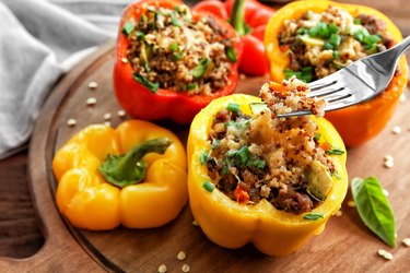 Red, yellow and orange bell peppers stuffed with quinoa, sitting on a wooden board