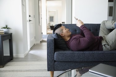 Man relaxing, using smart phone on living room sofa