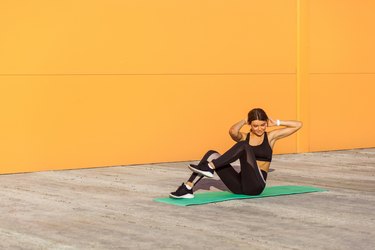 Young sporty woman swing press practicing, doing crisscross exercise, bicycle crunches pose, working out, in sportswear, black pants and top