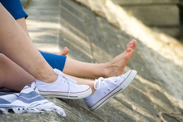 Close-up of legs in sneakers and bare feet on a granite promenade, selective focus