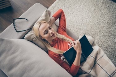 High angle above view of a woman sleeping on the couch with a blanket after reading a book