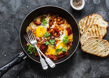 Shakshuka with baked sweet peppers and chickpeas in frying pan on a dark background, top view
