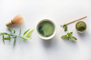 Ceremony green matcha tea and bamboo whisk on white concrete table. Top view.