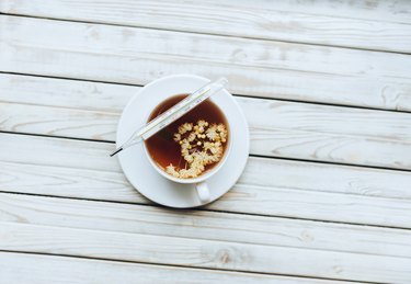 A mercury glass thermometer lies on a white cup with a linden, fragrant healing tea made from dried linden flowers on a grey wooden background.