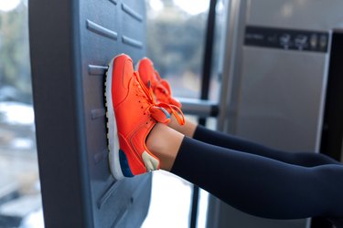 Slim smiling woman using a leg press machine and placing her legs on the platform