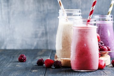 Selection of pink berry smoothies and milkshakes on a wooden table with striped paper straws surrounded by scattered loose berries