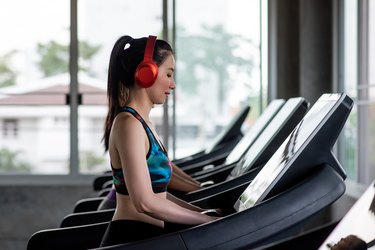 Side View Of Young Woman Wearing Red Headphones While Exercising On Treadmill In Gym