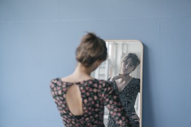 Young woman in vintage dress looking into mirror