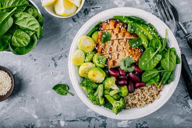 Healthy buddha bowl lunch with grilled chicken, quinoa, spinach, avocado, brussels sprouts, broccoli and red beans with sesame seeds