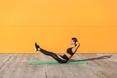 Young sporty attractive woman practicing yoga, doing paripurna navasana exercise, balance pose, working out, wearing sportswear, black pants and top.