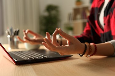 A woman meditating in front of her laptop at home