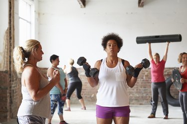 Female fitness trainer instructing woman lifting dumbbells