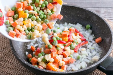 Mixed frozen vegetables in a frying pan on wood table