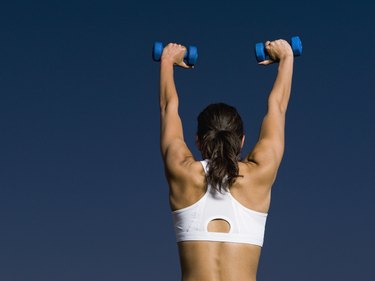 Rear view of mixed race woman holding dumbbells overhead