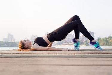 Young happy sporty woman mother working out, doing butt bridge