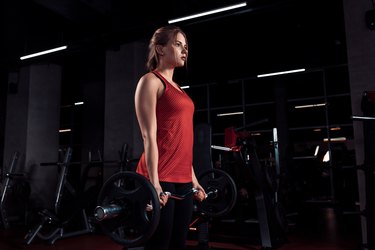 Young beautiful woman doing exercise with bar in a gym. Athletic girl doing workout in a fitness center.
