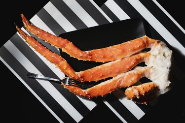 Crab legs and fork in black plate on black and white striped background, view from above