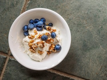 Ceramic bowl with yogurt, crushed walnuts and blueberries on a granite countertop