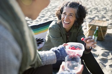 Smiling women eating raspberries at a beach picnic