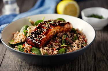 Healthy brown rice salad for weight loss with grilled teriyaki  salmon fillet in a gray bowl resting on wooden tabletop