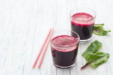 Fresh beet juice in glasses with a straw on a light blue background