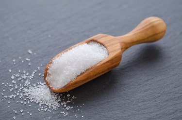 xylitol or birch sugar in a wooden scoop on black background, selective focus