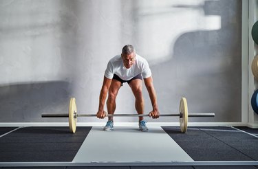 Fit senior man lifting weights alone in a gym