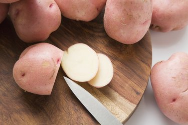 Red potatoes, one partly sliced, on wooden board
