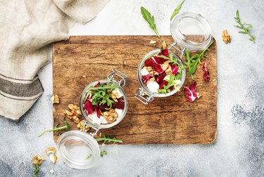 Beet salad with fresh arugula, soft goat cheese and walnuts, trendy salad jar, steel fork, gray kitchen table background, wooden cutting board, copy space, top view