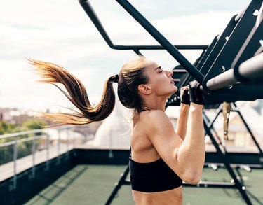 Female athlete exercising chin-ups. Side view of young woman doing workout on a roof terrace.