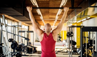 Close up back view of motivated and focused strong muscular active healthy young bald man working pull ups in the modern gym.