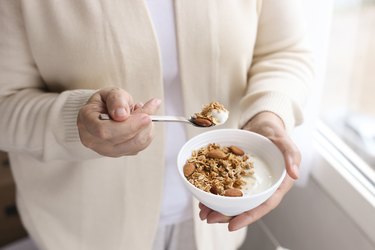 An unrecognizable woman eating a bowl of yogurt with granola and almonds on top