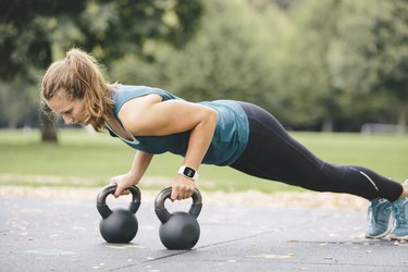 Young woman going pushups on kettlebells