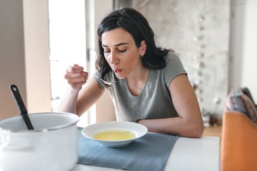 young woman eating soup at home, as an example of how to relieve wisdom tooth pain by eating soft foods