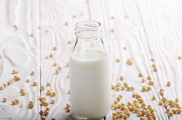 Non-dairy alternative Soy milk or yogurt in glass bottle on white wooden table with soybeans aside