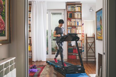 Adult with short dark hair walking on a treadmill in the living room wearing bright pink tennis shoes