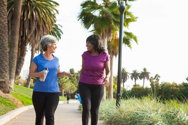 Female friends walking in park for exercise, holding water bottles