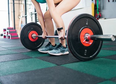 Strong young fit woman doing deadlift with a barbell in the gym. Free weight training