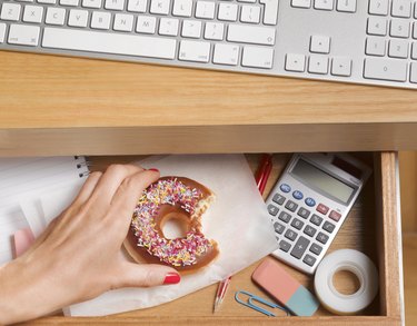 A woman's hand reaching for a doughnut in her desk drawer