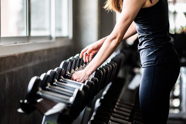 A young woman picking up a set of dumbbells from a rack at the gym