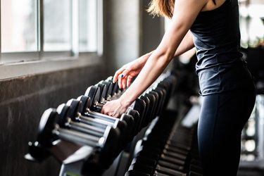 Person picking up a set of dumbbells from a rack at the gym