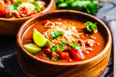 Traditional mexican bean soup with meat and cheese in wooden bowl, dark background