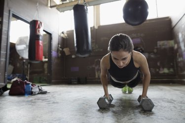 Strong boxer doing push up exercise with dumbbells at gym