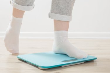 female legs on electronic scales on  wooden floor