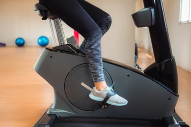 Low Section Of Woman Cycling On Exercise Bike In Gym