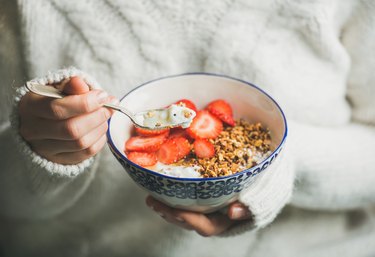 A woman holding a bowl of unprocessed yogurt, granola, and strawberries
