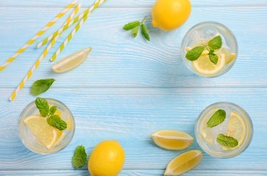 Cold refreshing summer drink with lemon and mint on light blue wooden background.