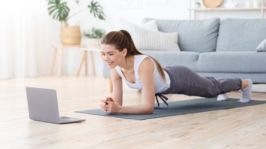 young woman doing a forearm plank at home in front of a laptop