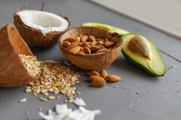 Healthy food concept with avocado, coconuts, almonds and oatmeal over gray background near window